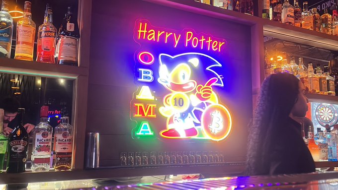 A bar counter displays a neon sign for "Harry Potter" and the number 10, with a person standing behind it.
