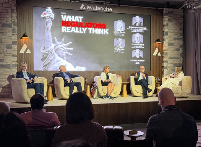A panel discussion titled "What Regulators Really Think" takes place at the Avalanche Summit in New York, featuring former SEC and CFTC commissioners (including Elad Roisman, J. Christopher Giancarlo, Troy Parades, and Caroline Crenshaw) seated on stage while engaging with the audience on cryptocurrency regulation. The image relates to the post by visually showcasing the timely "spicy" panel conversation about regulatory boundaries and SEC innovation exemptions following the summit.
