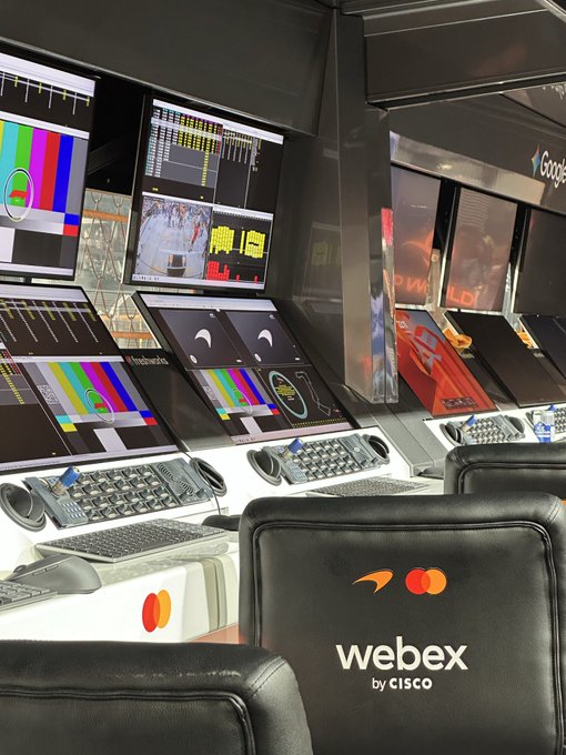 A workstation or control room with multiple monitors showing Google interfaces and test patterns, accompanied by keyboards and a chair branded with the 'webex by CISCO' logo.