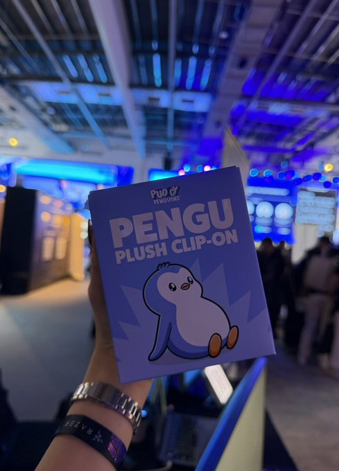 A hand proudly displays a "PENGU PLUSH CLIP-ON" box from Pudgy Penguins, with the Pudgy Penguins branding visible at the top, capturing the excitement of receiving the NFT merchandise drop from @jyp_nft.