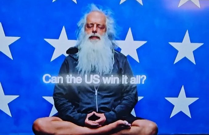 The image shows an older man with a long white beard meditating in a lotus position against an American flag backdrop, with text overlay reading "Can the US win it all?"—apparently a Polymarket advertisement featuring Rick Rubin in a satirical pose that contrasts with his known minimalist, Zen-like persona.