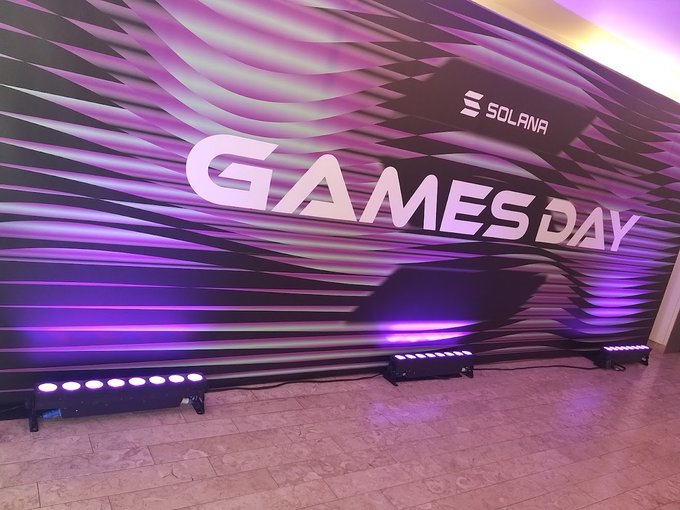 A vibrant purple and white wavy backdrop displaying 'SOLANA' and 'GAMES DAY' text, illuminated by stage lights on the floor.