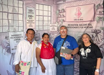 Four people stand in front of a mural reading '100+ startups 200+ investors' and 'INNOVATION: BUILDING REAL IMPROVEMENTS FOR MEXICANS,' with one man holding a folder.