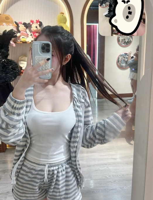 A young woman in striped pajamas takes a mirror selfie while holding a strand of her long hair, with plush toys visible in the background. The image accompanies a casual Thursday greeting post promoting VanGrid IO, seemingly using the selfie as a relatable personal touch to connect with viewers.
