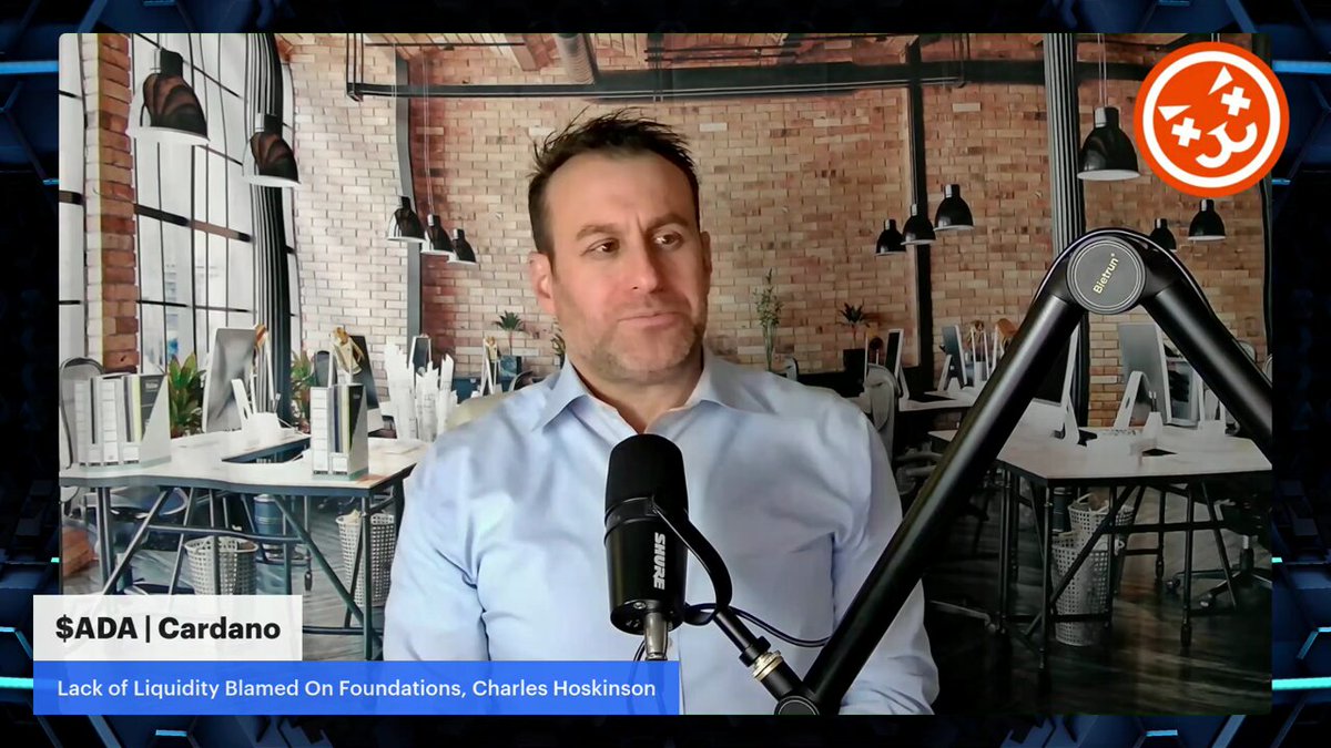 The image shows a man wearing a blue shirt sitting at a desk with a microphone in front of him. The background features a brick wall and several desks arranged around the room, suggesting an office setting. The caption reads "Focus on what is in the image and how it relates to the post".