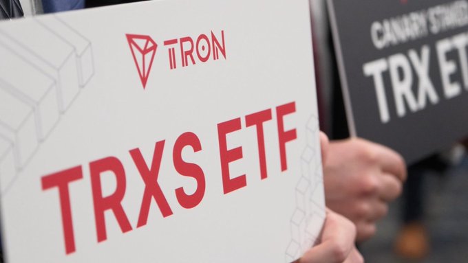 The image shows hands holding promotional signs reading "TRX S ETF" with the TRON logo and "CANARY STAKED TRX ETF" branding, celebrating TRON's listing on a U.S. exchange via Canary Capital's newly launched staked TRX ETF.