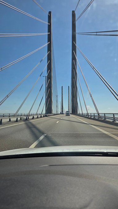 A car drives across a large cable-stayed bridge under a clear blue sky, likely the Øresund Bridge connecting Denmark to Sweden, matching the post's "off to Sweden" journey.