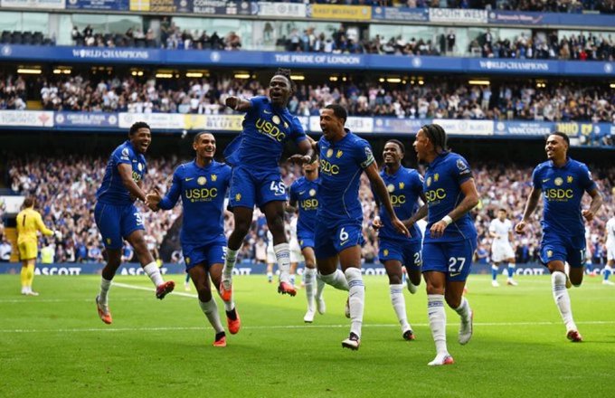 Chelsea FC players in blue "USDC" sponsored jerseys celebrate a goal at Stamford Bridge, promoting the new @ChelseaFC x @USDC kit collaboration now available online and in-stores. The "USDC" logo (referencing the USD Coin cryptocurrency ticker) is prominently displayed across the front of the team's kits.