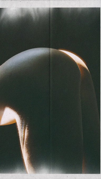 A dark, grainy photo of a curved sculpture or object with light catching its edges against a black background.