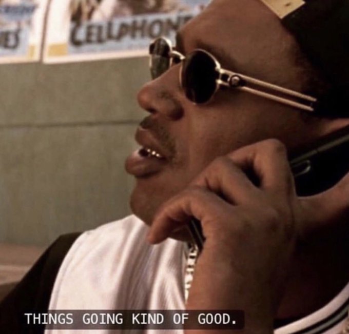 A man wearing round sunglasses and a white t-shirt is talking on a mobile phone, with the caption "THINGS GOING KIND OF GOOD." displayed at the bottom.