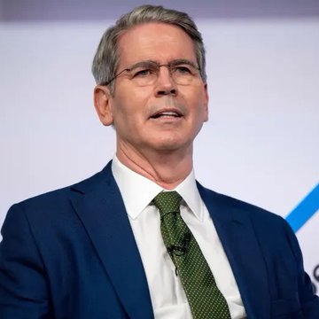 Scott Bessent, U.S. Treasury Secretary, speaks at a podium wearing a navy suit and green tie, pictured in connection with the Treasury's announcement of a potential $1 trillion debt buyback program that could lower bond yields and benefit Bitcoin.