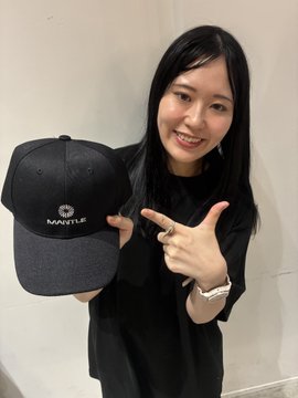 A smiling woman with long dark hair holds up a black cap with a "NANTU" logo and points to it with her finger.