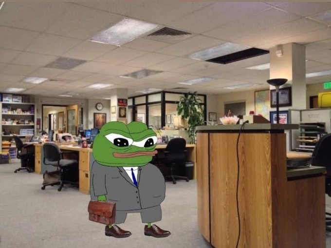 A Pepe the Frog character dressed in a gray business suit and carrying a briefcase stands inside a typical office environment.