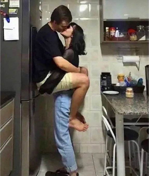 A man lifts a woman off the ground to kiss her passionately in a kitchen, with his back against the refrigerator as he holds her up by her thighs. The image, paired with the caption about a "man date" booked through PayBox, humorously suggests the poster is celebrating a romantic date funded by the payment service.