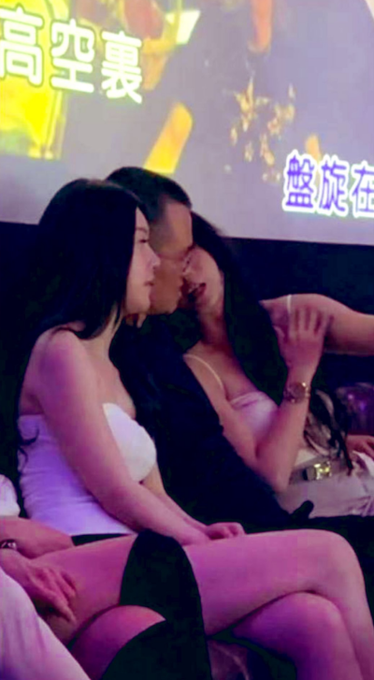 A man kissing two women at what appears to be a club or event with Chinese text including '高空轰' and '螺旋轰' visible on screens in the background.