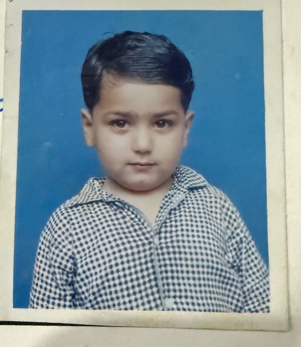 A vintage portrait of a young child with neatly combed dark hair, wearing a blue and white checkered shirt against a blue background, humorously presented as "the kid who runs this account."