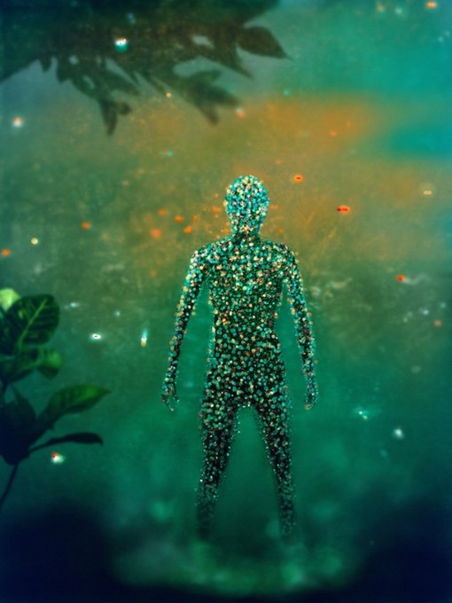 An artistic image shows a human figure composed entirely of sparkling, jewel-like textures standing in a greenish, ethereal environment with floating lights.