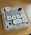 A small white mechanical keypad with circular keys and a digital display, sitting on a wooden surface.