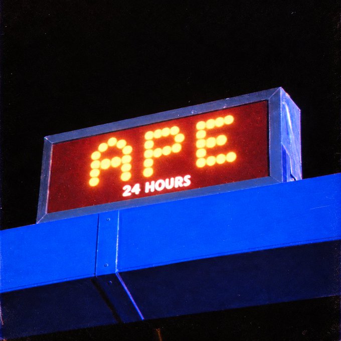 An illuminated digital gas station sign displays "APE" in bright orange LED lights with "24 HOURS" written below, mounted on a blue canopy against a black night sky—visually reinforcing the post's $APE ticker reference and conveying round-the-clock energy for the "just getting started" message.