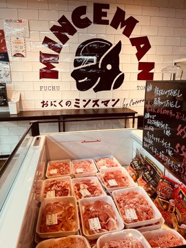 A storefront at "MINCEMAN" (おにくのミンスマン) in Fuchu, Tokyo displays neatly packaged cuts of minced meat in a refrigerated case, with a chalkboard listing "Hauserl" and other items. The pun-friendly shop name—blending "mince" (ground meat) with a gladiator mascot—makes it an ideal comedic setting for the poster's quip about JPYC stablecoin payments.