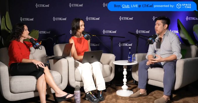 The image features three people sitting around a table, engaged in conversation. They appear to be discussing something related to ethical finance or open finance. One person is seated at the head of the table, while two others are positioned towards the right side. The background includes a banner with the text "Ethical Finance" and "Open Finance", indicating that this gathering might be taking place at an event like @ethconf. Additionally, there's a bottle on the table near one of the individuals.