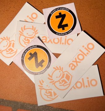 A pile of stickers and paper items featuring the orange Axolotl.io logo (a smiling axololotl mascot) and the Zcash cryptocurrency logo with text 'Zcash on axololotl'.
