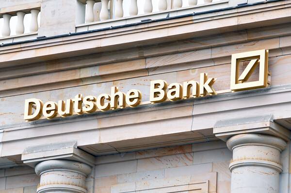 The image shows the gold-lettered "Deutsche Bank" signage with its distinct slash logo mounted on a sandstone building façade. The caption relates to the article's announcement that Deutsche Bank plans to launch crypto custody services in Germany.