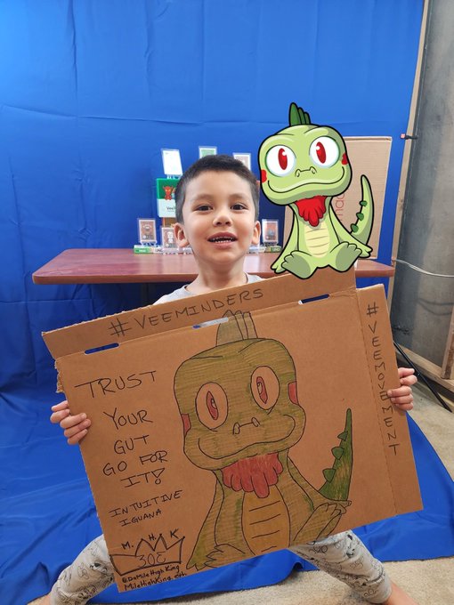 Boy holding cardboard sign with dragon drawing, text '#VEEMINDERS TRUST YOUR GUT FOR ITS INTUITIVE IQ'