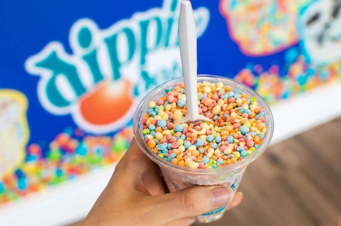 A hand holds a clear cup filled with colorful Dippin' Dots ice cream, with the brand's blue logo visible in the background. The image perfectly captures the playful spirit of the caption, showcasing the signature "dots" of the popular ice cream treat.