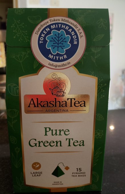 A box of Akasha Tea Argentina "Pure Green Tea" featuring 15 large leaf pyramid tea bags, distributed through Mithrandir Token (info@mithr.io). The packaging displays the brand's branding alongside a sticker promoting Token Mithrandir ($MITHR), tying into the post's focus on Akashas pyramid tea bags and the Mithr token ecosystem.