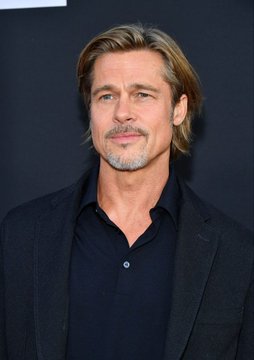 A portrait of Brad Pitt, a famous actor with shoulder-length blonde hair and a goatee, wearing a dark blazer over a black shirt.