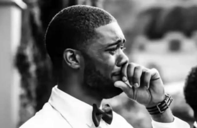 A black-and-white photo of a bearded man in a bow tie, appearing thoughtful or contemplative with his hand near his mouth.