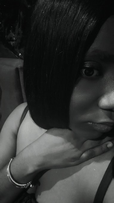 A black-and-white selfie of a young woman with long dark hair, wearing a tank top and a bracelet, resting her chin on her hand.