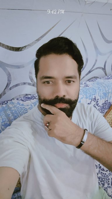 A bearded man in a white t-shirt poses with his hand on his chin against a blue and white patterned backdrop, with "9:42 PM" displayed at the top. The thoughtful pose complements the post's contemplative tone about Tria solving crypto's scattered ecosystem problem.
