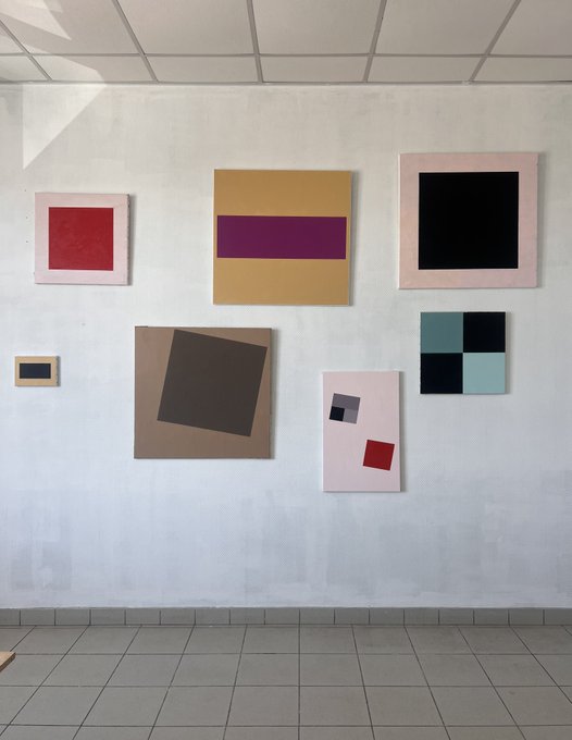 Seven abstract paintings, inspired by CryptoPunk quotes, are displayed on a new studio wall. The collection features various geometric shapes and color combinations, representing the unique traits of each CryptoPunk.