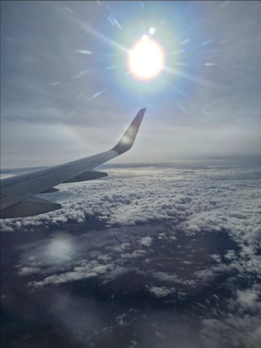 An airplane wing soars above a vast expanse of clouds with the sun brightly shining overhead, capturing the essence of rising above the turbulence to find the sun's clarity. The image visually echoes the post's message about maintaining clear vision and perseverance, much like Solana's "keep building, keep rising" ethos of ascending beyond challenges toward consistent growth.