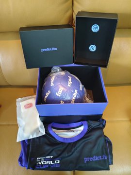 A purple Predict football and matching jersey are displayed in branded gift boxes alongside "predict.fun" and "PREDICT THE WORLD" packaging, showcasing the World Cup-themed merchandise set. The caption celebrates receiving this limited edition swag as part of the "Predict Cup" campaign tied to the 2026 World Cup with a $2M prize pool.
