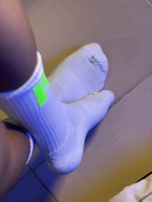The image features a person wearing white socks with green stripes, standing on a tiled floor. The person's feet are positioned in front of them, showcasing their socks. There is also a towel visible near the bottom right corner of the photo. The caption provided seems unrelated and does not seem to be directly related to the main subject - the person and their white socks with green stripes.