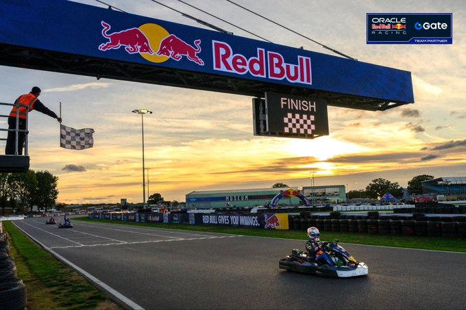 A Red Bull-sponsored go-kart crosses the finish line beneath a checkered flag and "Red Bull" overhead banner, with a finish light displaying the checkered pattern. The scene captures a historic racing moment as @Max33Verstappen celebrates starting from P101 and passing all competitors within 30 laps to claim victory.