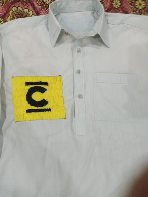 A light gray button-up shirt features a hand-embroidered yellow patch with the black "Concrete" logo (stylized "C" between two horizontal lines) on the left chest pocket area, representing the creator's wearable realization of their "I 💛 Concrete" concept for the @ConcreteXYZ community.