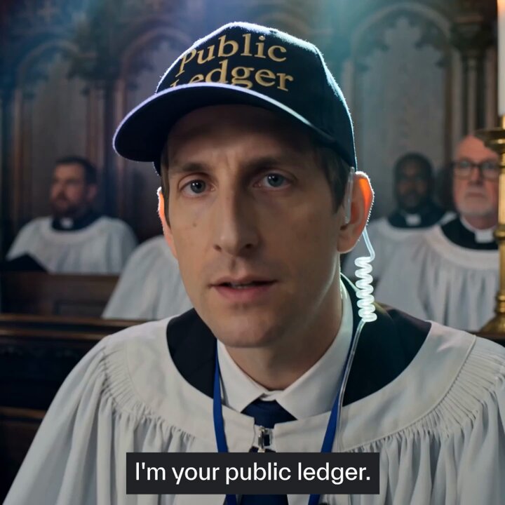 The image features a man wearing a white robe with a black hat, possibly a priest or a religious figure, standing in front of a group of people dressed in robes as well. They are all gathered around a table, which has a computer screen on top of it. The caption reads "I'm your public ledger." This suggests that the image is related to blockchain technology and its use for transparency and trust in financial transactions or other areas where information sharing is crucial.