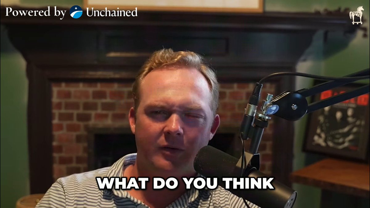 The image features a man wearing a striped shirt, holding a microphone with his right hand while looking at the camera. The background of the image shows a fireplace and a picture frame. There are also some words visible in the image that read "What do you think".