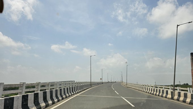 A view from a vehicle driving on a paved road across a bridge, with concrete railings and streetlights under a partly cloudy sky.