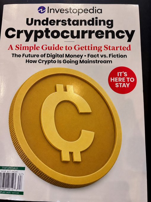 The image shows an Investopedia magazine titled "Understanding Cryptocurrency: A Simple Guide to Getting Started," featuring a large gold coin emblem on the cover along with a red "It's Here to Stay" badge. The accompanying post recommends this beginner-friendly publication as helpful reading material for those new to crypto, aligning perfectly with the magazine's subtitle about getting started in the world of digital currency.
