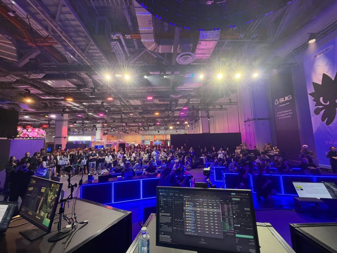 A Sui Foundation panel reveals the SWIFI launch to a packed crowd at an indoor event space, with production monitors and stage lighting in the foreground capturing the announcement.