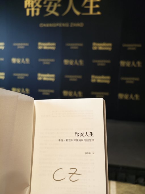 A signed copy of CZ’s book 《幣安人生》 is open to a personalized page showing his signature, with a “CHANGPENG ZHAO” event backdrop behind it. The photo highlights the fan’s front-row access to the Binance founder and a signed copy of his book.