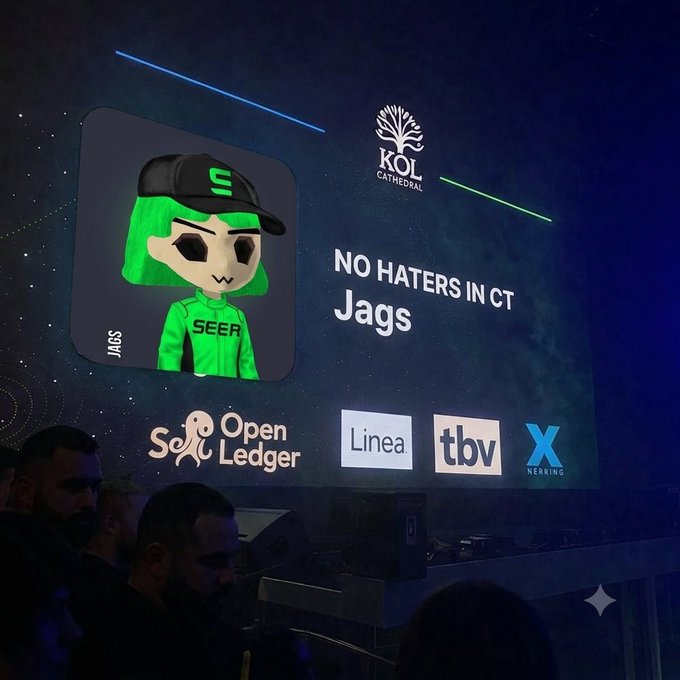 A photo of a presentation screen at KOL Cathedral showing a digital avatar named 'Jags' with green hair and a 'SEER' shirt, under the heading 'NO HATERS IN CT', with logos for OpenLedger, Linea, tbv, and X Layer below.