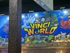 The image shows a large mural of a cartoon character from the video game "Vinci World" displayed at a convention center or exhibition. The mural features various characters and elements that are part of the game's theme, such as buildings, trees, and other objects. The booth is set up with a sign that reads "Vinci World", indicating its purpose for attendees to explore and enjoy. The image also includes text that provides information about the event or the booth, suggesting it is an important aspect of the convention experience.