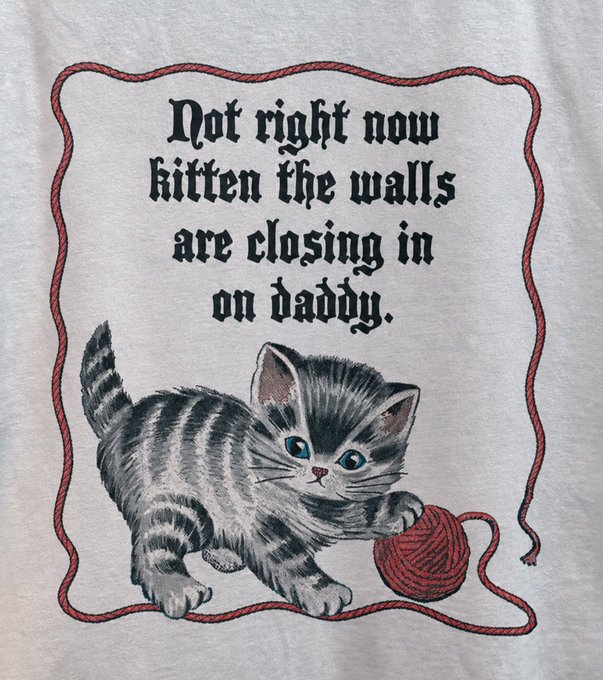 A vintage-style graphic printed on a light gray fabric featuring an illustration of a gray tabby kitten playing with a red ball of yarn, accompanied by the text "Not right now kitten the walls are closing in on daddy." framed by a decorative red rope border.