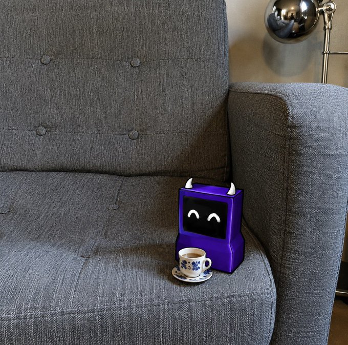A small purple robot figurine with white horns and a smiling digital face sits on a gray tufted couch next to a delicate blue-and-white teacup, with a metallic lamp visible in the background.